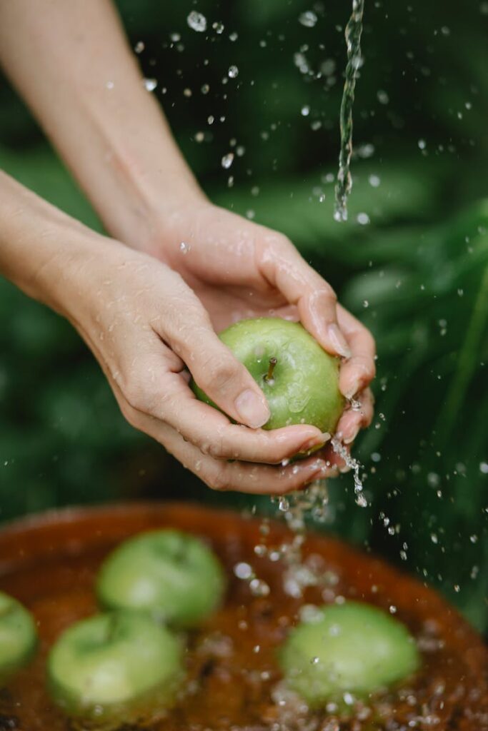 Close-up of hands washing a fresh green apple under running water, emphasizing cleanliness and freshness.