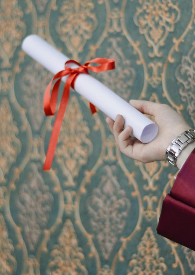 A graduate's hand holding a diploma with red ribbon, symbolizing achievement.